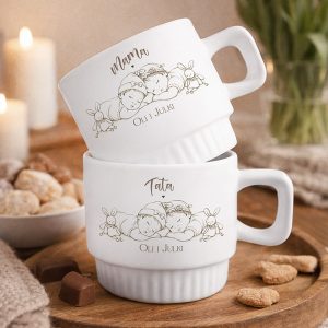 Dwie białe filiżanki z rysunkami dzieci śpiących obok króliczków, napisy „Mama” i „Tata”, imiona dzieci.