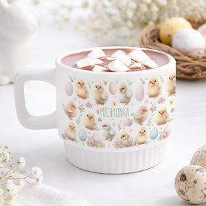 Personalizowany biały kubek z zabawnym wzorem kurczaczków i kwiatuszków, napełniony gorącą czekoladą, ozdobiony piankami marshmallow.