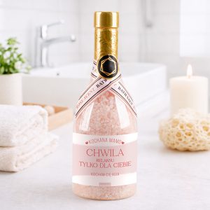 Butelka na sól do kąpieli z różowym etykietą, napis "CHWILA RELAKSU TYLKO DLA CIEBIE", w romantycznym otoczeniu z świecą i gąbką.