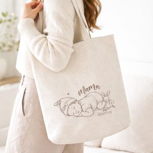 Kobieta w swetrze trzyma torbę z rysunkiem niemowlęcia i napisem "Mama".
