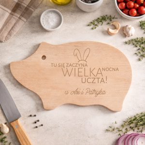 Deska do krojenia w kształcie świni, z napisem "TU SIĘ ZACZYNA WIELKA NOCNA UCZTA!" oraz imionami.