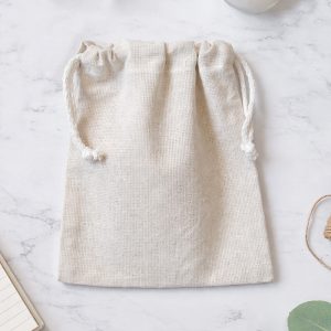 Beżowy woreczek z lnianego materiału ze sznurkiem, leżący na marmurowym blacie.