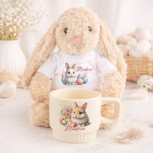 Pluszowy królik siedzi obok filiżanki z rysunkiem królika i dekoracjami wielkanocnymi. Zestaw prezentowy personalizowany.