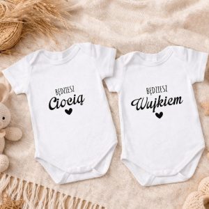 Body dla dzieci z napisami "Będziesz Ciocią" i "Będziesz Wujkiem" na białym tle, na tle naturalnych tkanin i zabawki.