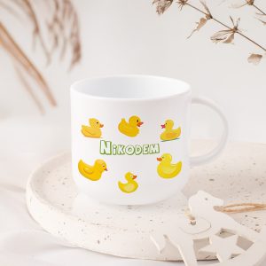 kubek-z-imieniem-dziecka-kaczuszki-personalizowany.jpg Biała filiżanka z żółtymi kaczkami i imieniem na środku, umieszczona na jasnym talerzu.