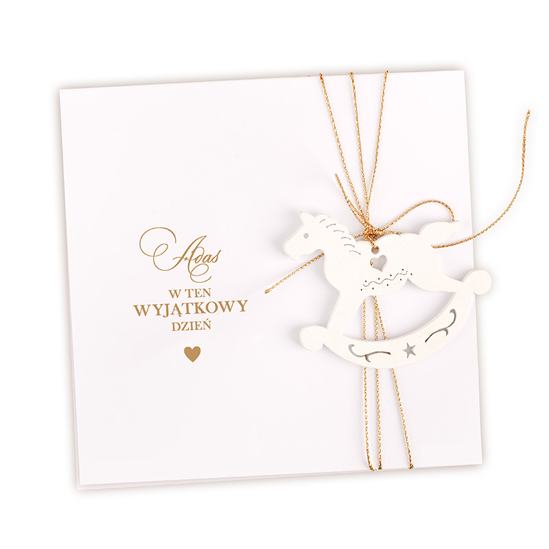 Biała kartka z złotym napisem "w ten wyjątkowy dzień" oraz dekoracją w postaci białego konika na huśtawce.