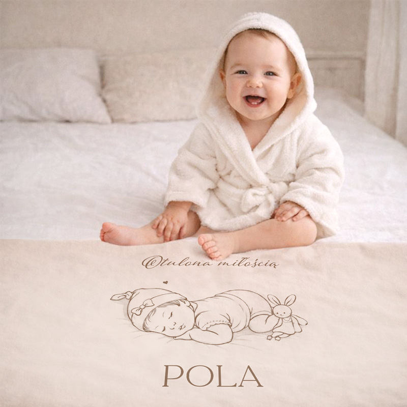 Uśmiechnięte niemowlę w kąpielowym szlafroku siedzi na łóżku, z kocem z rysunkiem śpiącego dziecka i napisem.