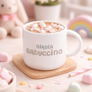 plastikowy-kubek-dla-dziecka-z-napisem-babyccino.jpg Biały kubek z napisem "Babyccino", na gorącym napoju z bitą śmietaną i różowymi piankami w otoczeniu cukierków.