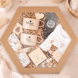prezent-dla-noworodka-z-kubkiem.jpg Zestaw prezentowy w kształcie sześciokąta zawierający kubki z napisami "MAMA" i "TATA", body dla dziecka, kocyk, kawę oraz dekoracyjne elementy.