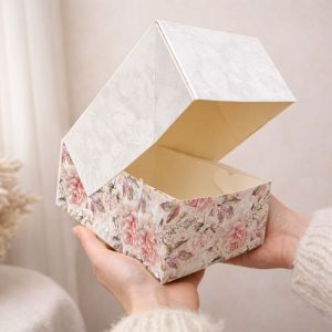 pudelko-kartonowe-na-ciasto-slodycze-upominki-motyw-kwiatow.jpg Otwarta, ozdobna pudełko z kwiatowym wzorem, trzymane w dłoniach na jasnym tle.