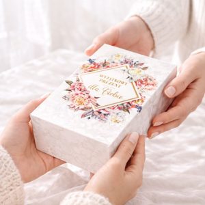 Dwie dłonie przekazują sobie ozdobne pudełko z napisem „Wyjątkowy prezent dla Ciebie” i kwiatowym wzorem.