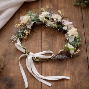 wianek-z-kwiatow-subtelny-wzor-ozdoba-glowy-na-komunie.jpg Wianek z kwiatów w delikatnych odcieniach bieli i zieleni, ozdobiony wstążką. Położony na drewnianym stole.