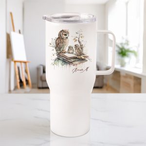 Kubek termiczny z ilustracją sów na książce, stojący na marmurowym blacie w jasnym pomieszczeniu.