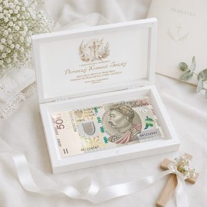 Biała szkatułka z banknotem 500 złotowym, ozdobiona kwiatami i krzyżem, w tle kartka z napisem "PAMIĄTKA".