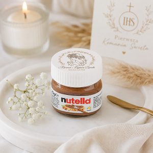 Słoiczek Nutelli na talerzu, obok drobne kwiaty i świeca, na tle eleganckiego kartki z napisem.