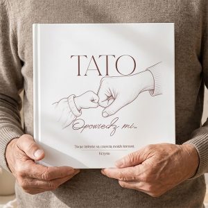 ksiazka-wspomnien-z-elegancka-twarda-oprawa-i-miejscem-na-historie.jpg Osoba trzymająca książkę "Tato, opowiedz mi..." z ilustracją rąk dziecka i ojca, w jasnym otoczeniu.