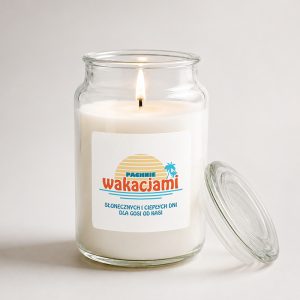 A lit candle in a glass jar with a label that reads "Pachnie wakacjami," featuring a sunrise and palm trees.