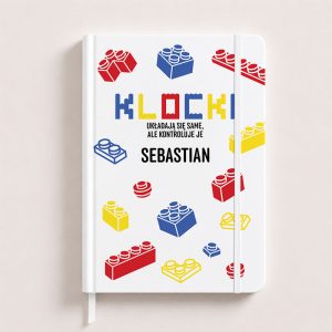Personalizowany biały notatnik dla fana klocków z imieniem, ozdobiony kolorowymi grafikami czerwonych, niebieskich i żółtych klocków.