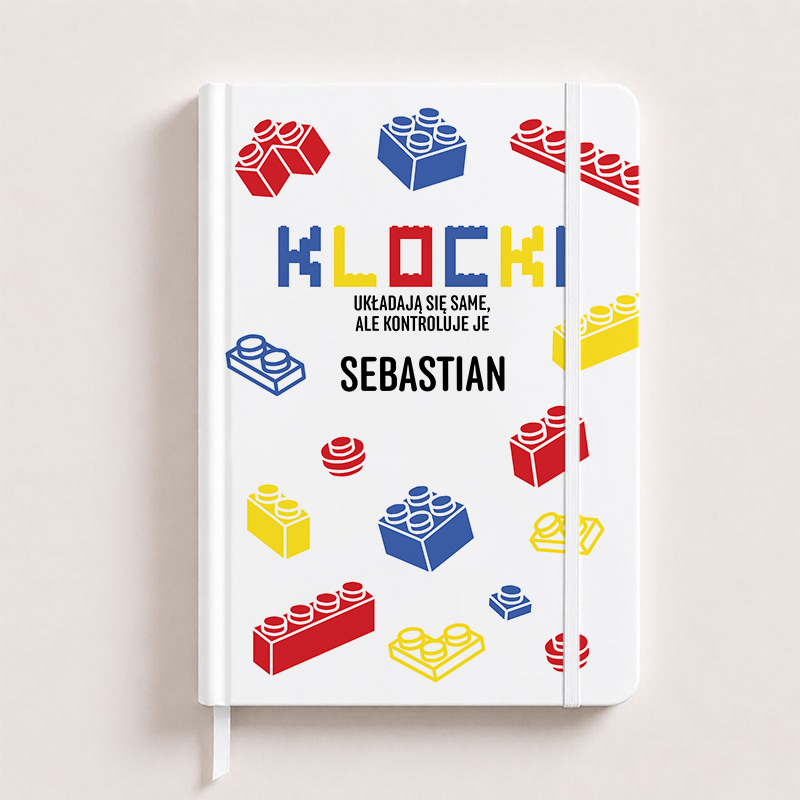 Personalizowany biały notatnik dla fana klocków z imieniem, ozdobiony kolorowymi grafikami czerwonych, niebieskich i żółtych klocków.